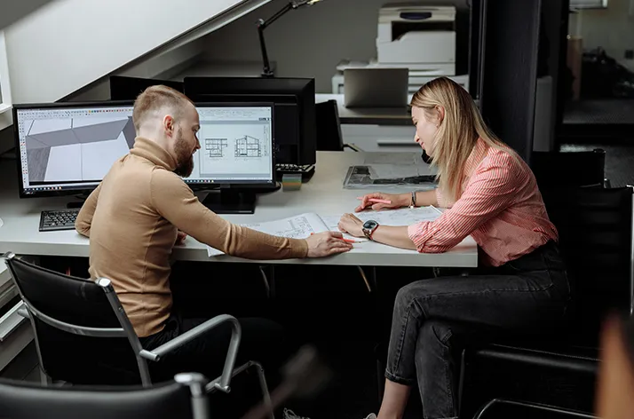 Team reviewing blueprints and 3D models on a computer during a design meeting.